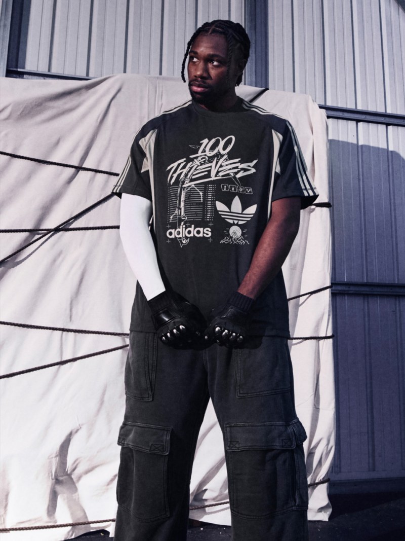 A man wearing a black and white Adidas t-shirt stands in front of a white curtain backdrop.