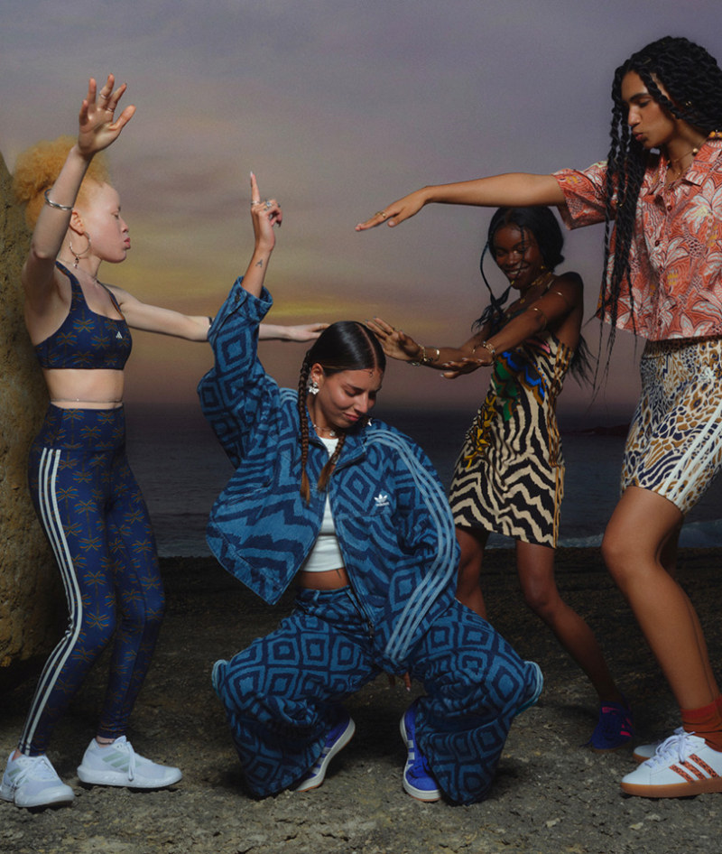 A group of young people, dressed in vibrant, patterned clothing, are engaged in a lively dance performance against a backdrop of a scenic outdoor setting.