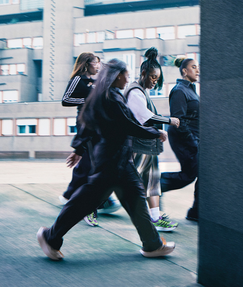 A group of people, some wearing athletic clothing, are walking quickly through an urban setting with buildings and structures in the background.