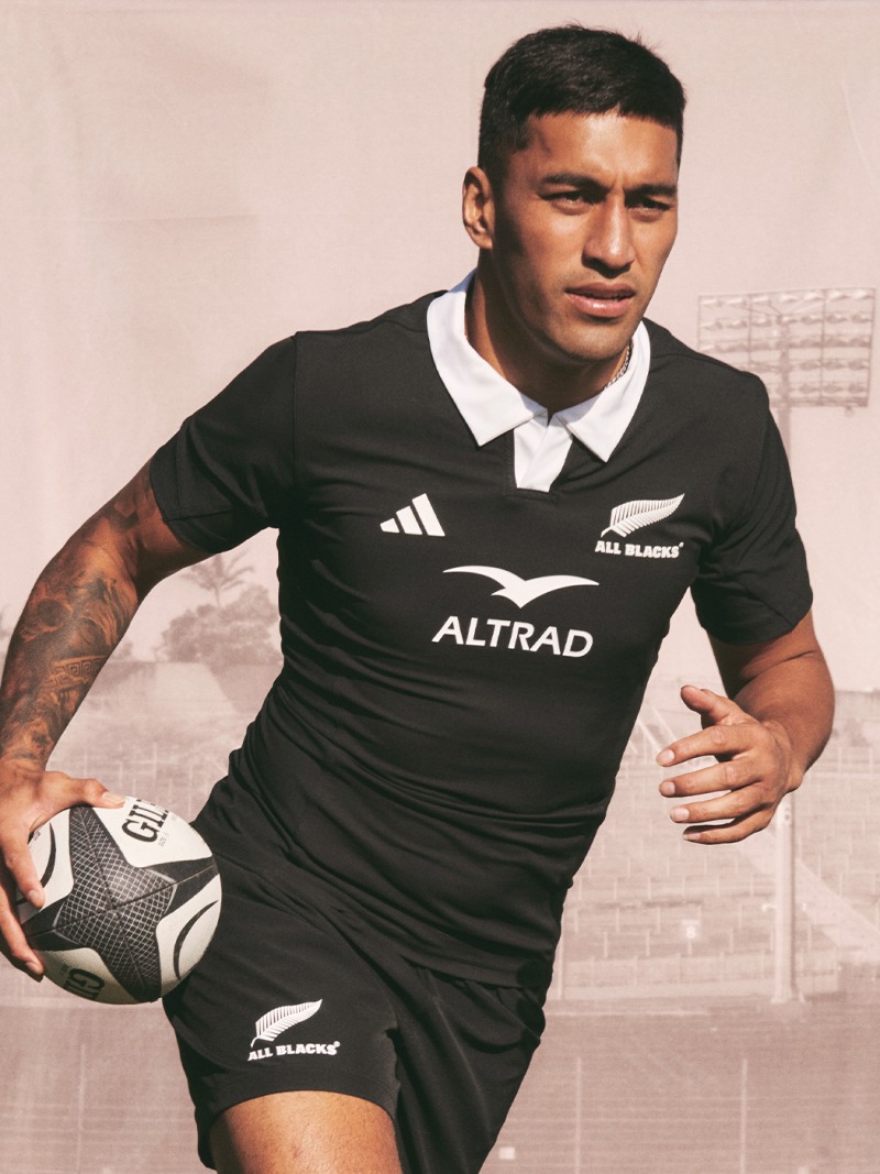 A young man wearing a black and white sports jersey is holding a soccer ball and standing in front of a blurred background.
