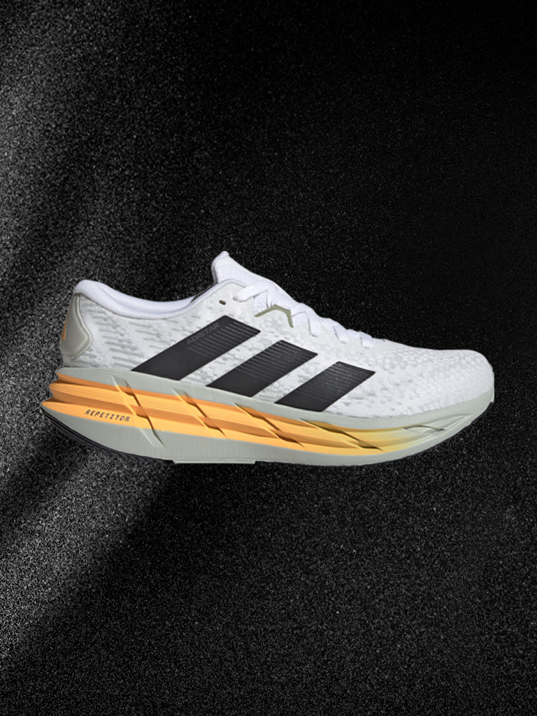 Une chaussure de sport blanche et orange avec des détails noirs est présentée sur un fond sombre.