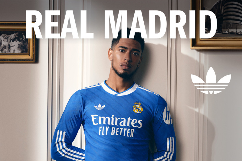 The image shows a young man wearing a blue Real Madrid soccer jersey standing in front of a wall with framed artwork.
