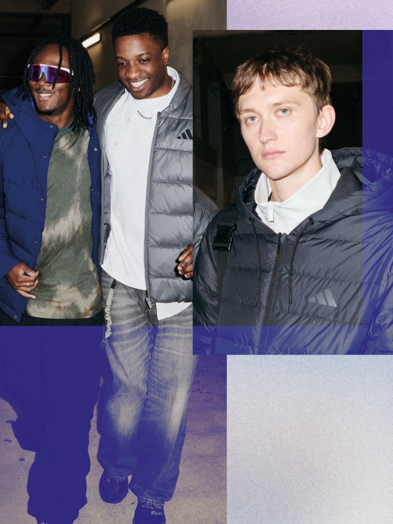 Das Bild zeigt drei junge Männer, die zusammenstehen, wobei einer eine blaue Jacke trägt, der andere ein weißes Hemd und der dritte eine graue Jacke. Der Hintergrund scheint in der Halle schwach beleuchtet zu sein.