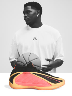 A young man wearing a white t-shirt is holding a basketball and standing in front of a pair of large, colorful sneakers.