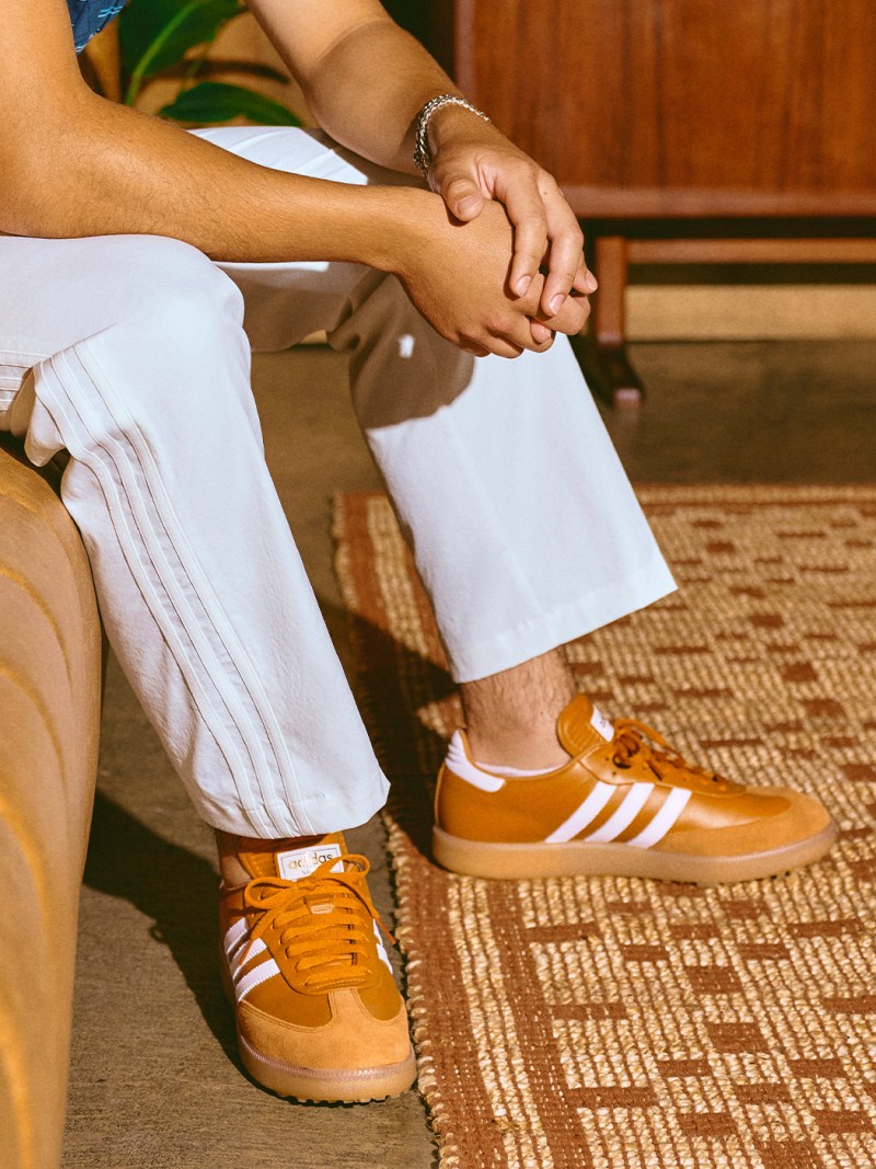The image shows a person's lower body, with their hands resting on their lap and wearing white socks and orange sneakers on a patterned floor.