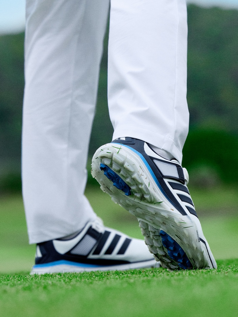 A pair of white and blue golf shoes standing on a lush green golf course.