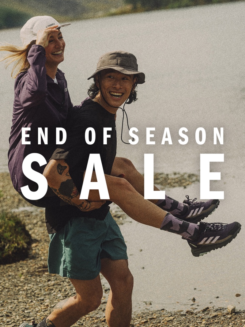 Two smiling individuals, a man and a woman, are running together on a dirt path surrounded by a grassy landscape, with the text "END OF SEASON SALE" overlaid on the image.
