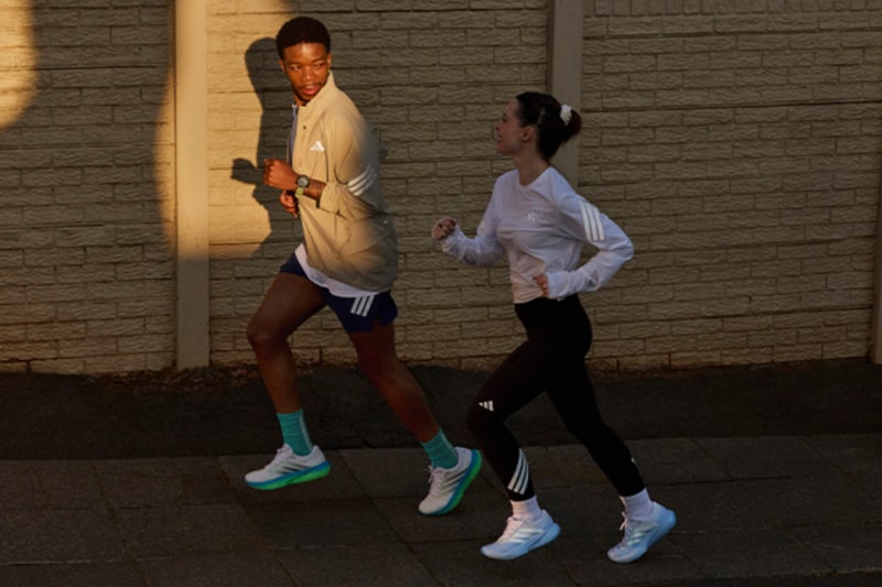 Two individuals, a man and a woman, are walking together at night against a backdrop of a brick wall.