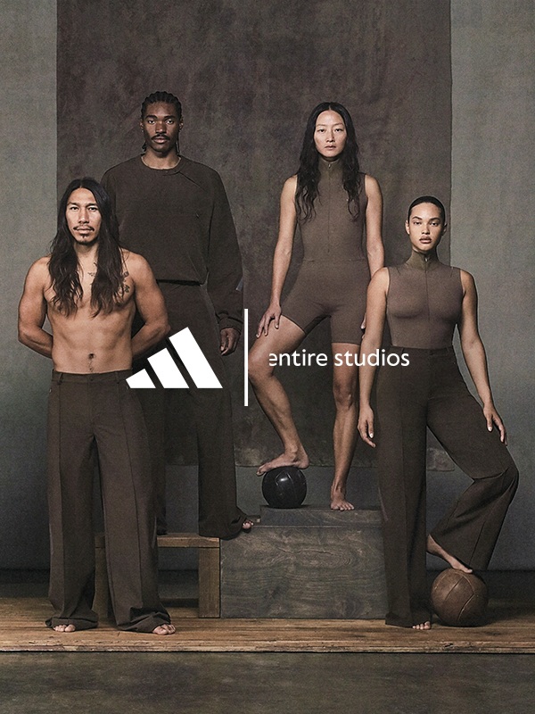 The image features four individuals, three men and one woman, standing together on a wooden platform against a plain background. The individuals are wearing minimal clothing, showcasing their physiques.