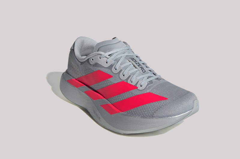 A gray and red athletic shoe with laces and the Adidas logo on a plain background.