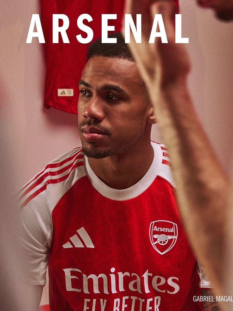 A young man wearing an Arsenal football jersey stands in a red-tinted environment, with the Arsenal logo prominently displayed on his jersey.