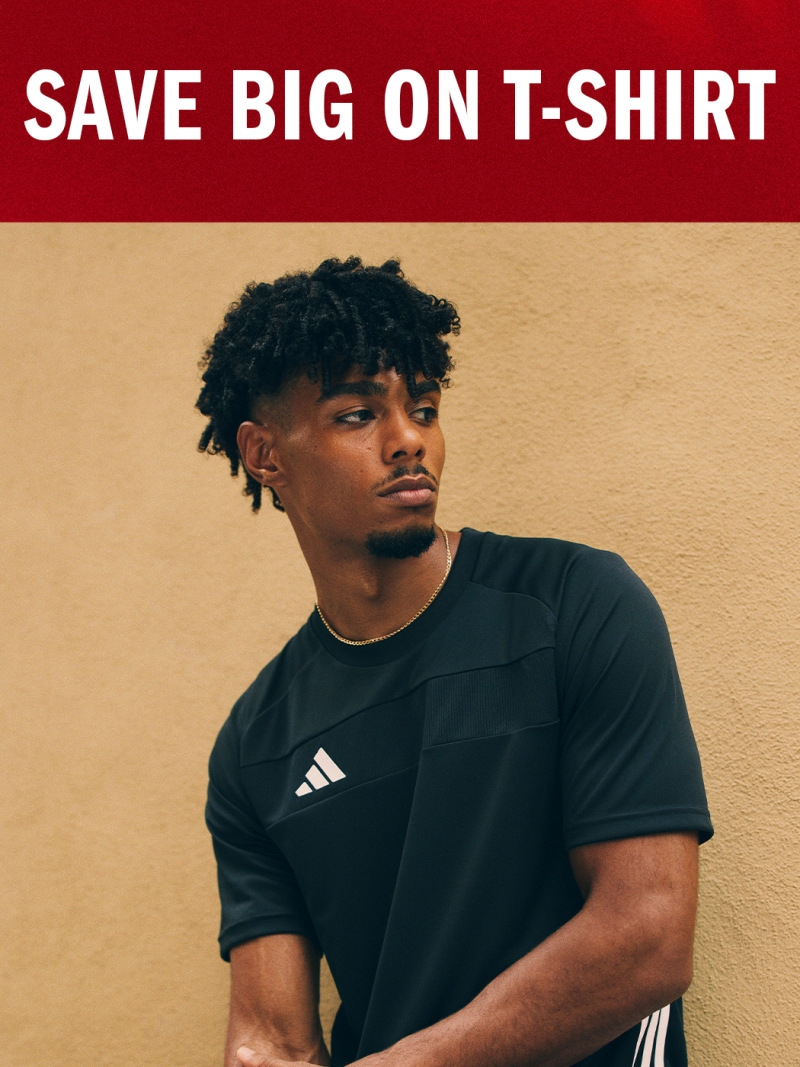 The image shows a young man with curly hair wearing a black t-shirt standing in front of a beige wall with a "Save Big on T-Shirt" text displayed prominently.