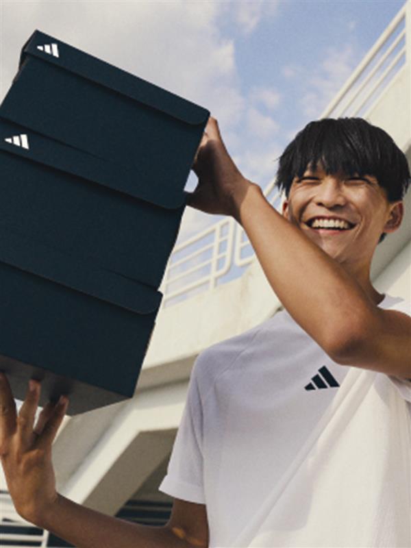 A woman carries 4 boxes of adidas sneakers on the background of a blue door