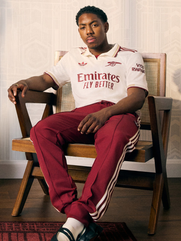 A young man wearing a white and red sports jersey is seated in a wooden chair against a plain background.