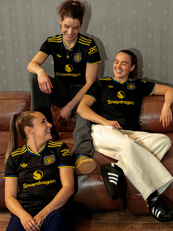 Three individuals, two women and one man, are seated on a couch wearing matching black and yellow jerseys with the "Snapdragon" logo. The background appears to be a plain, light-colored wall.