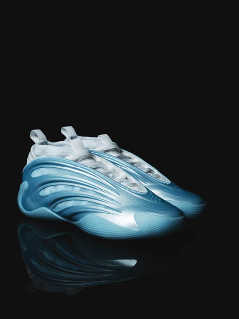 A pair of futuristic-looking sneakers in shades of blue and white, resting on a reflective surface against a dark background.
