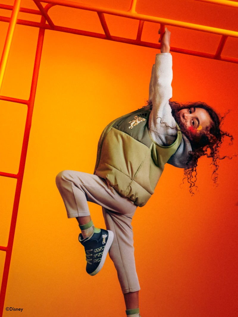 One child swinging from a monkey frame with a Simba shadow beside her, wearing the adidas | Lion King collection