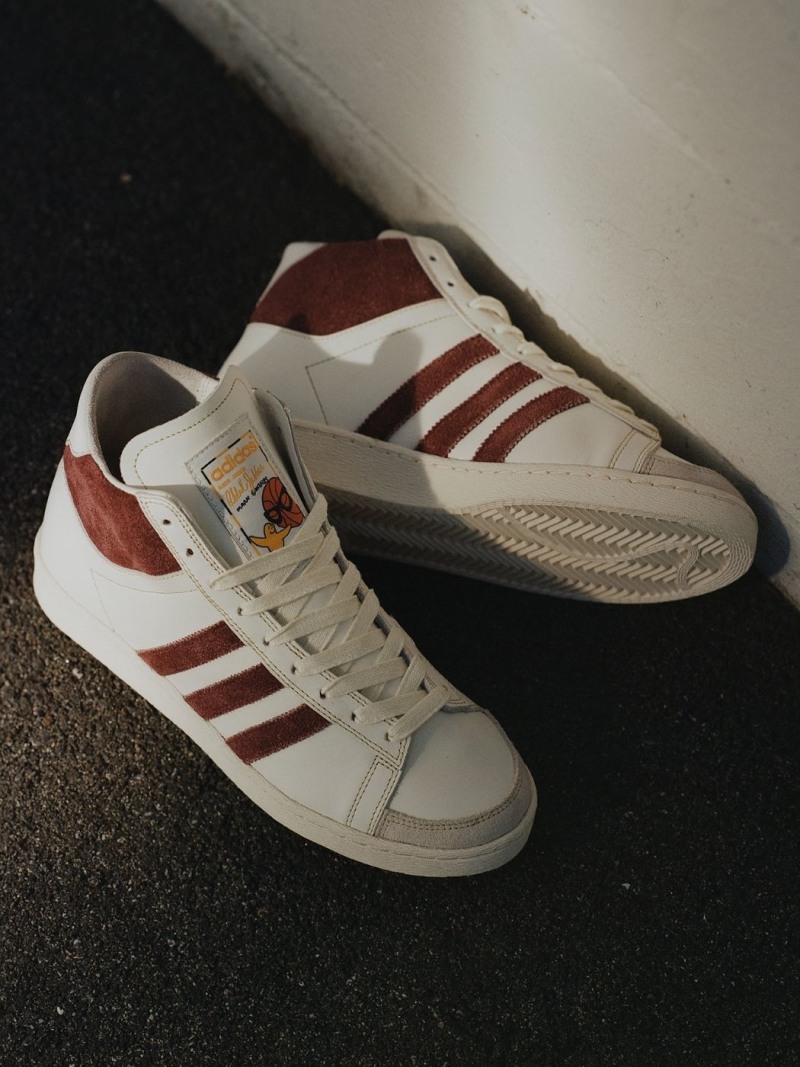 A pair of white and maroon sneakers with the Adidas logo are shown on a dark surface.
