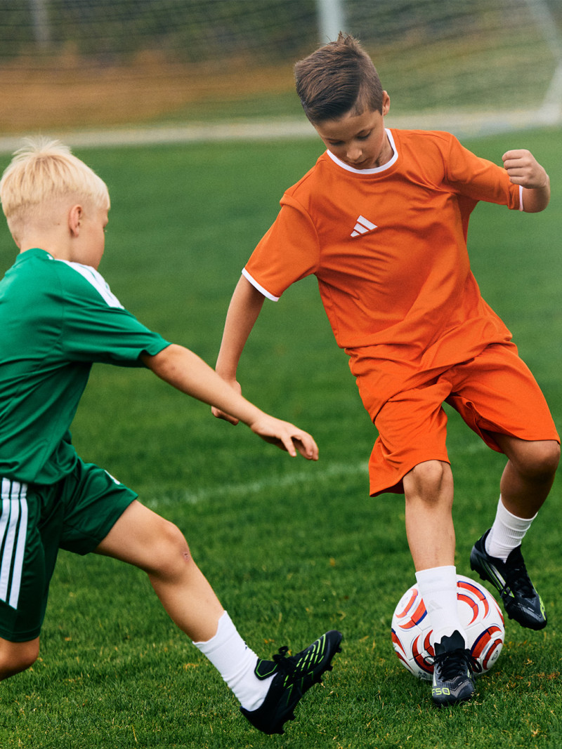 Two young boys in sports uniforms are playing soccer on a grassy field.