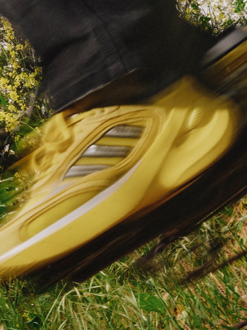 A yellow and black athletic shoe rests on a grassy surface, with blurred foliage visible in the background.