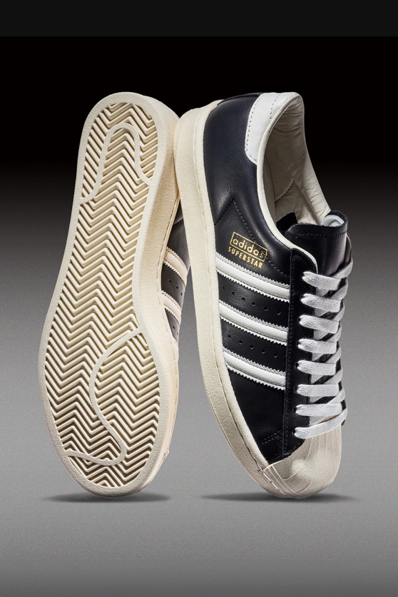 A pair of black and white Adidas sneakers with a distinctive treaded sole, set against a dark background.