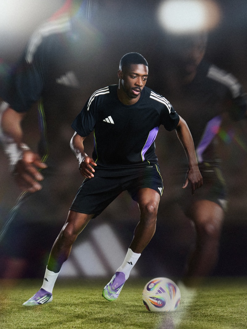 Un joueur de football en uniforme noir court avec le ballon sur un terrain faiblement éclairé, entouré de figures floues en arrière-plan.
