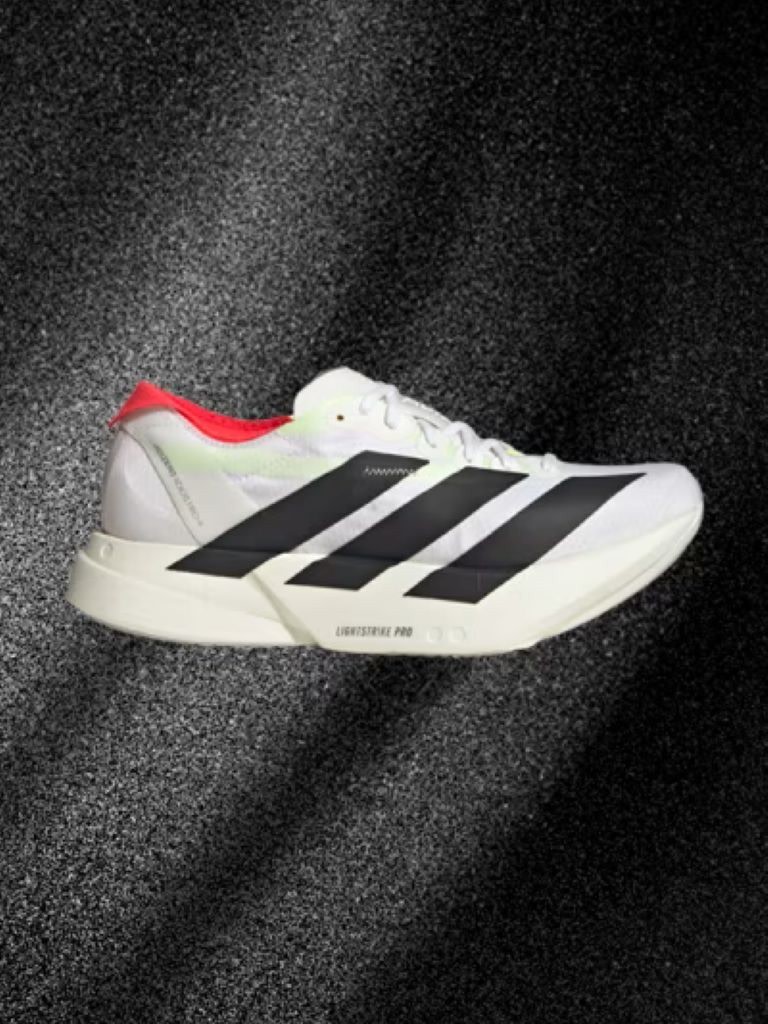 A white and black athletic shoe with red accents is displayed against a dark, textured background.