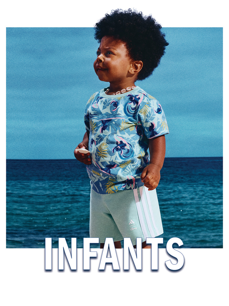 A young child with curly dark hair stands on a beach, wearing a colorful floral-patterned shirt, against the backdrop of a serene blue ocean.