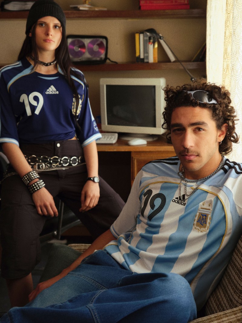 Two individuals, a man and a woman, are seated in a room with shelves and a television visible in the background. They are both wearing jerseys with the number 19 on them.