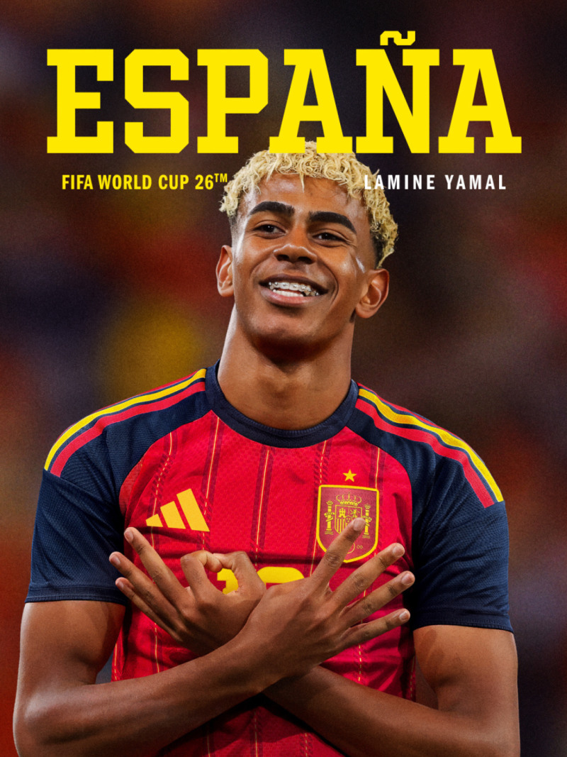 The image shows a smiling soccer player wearing a red and yellow jersey with the word "ESPANA" prominently displayed, standing against a dark background.