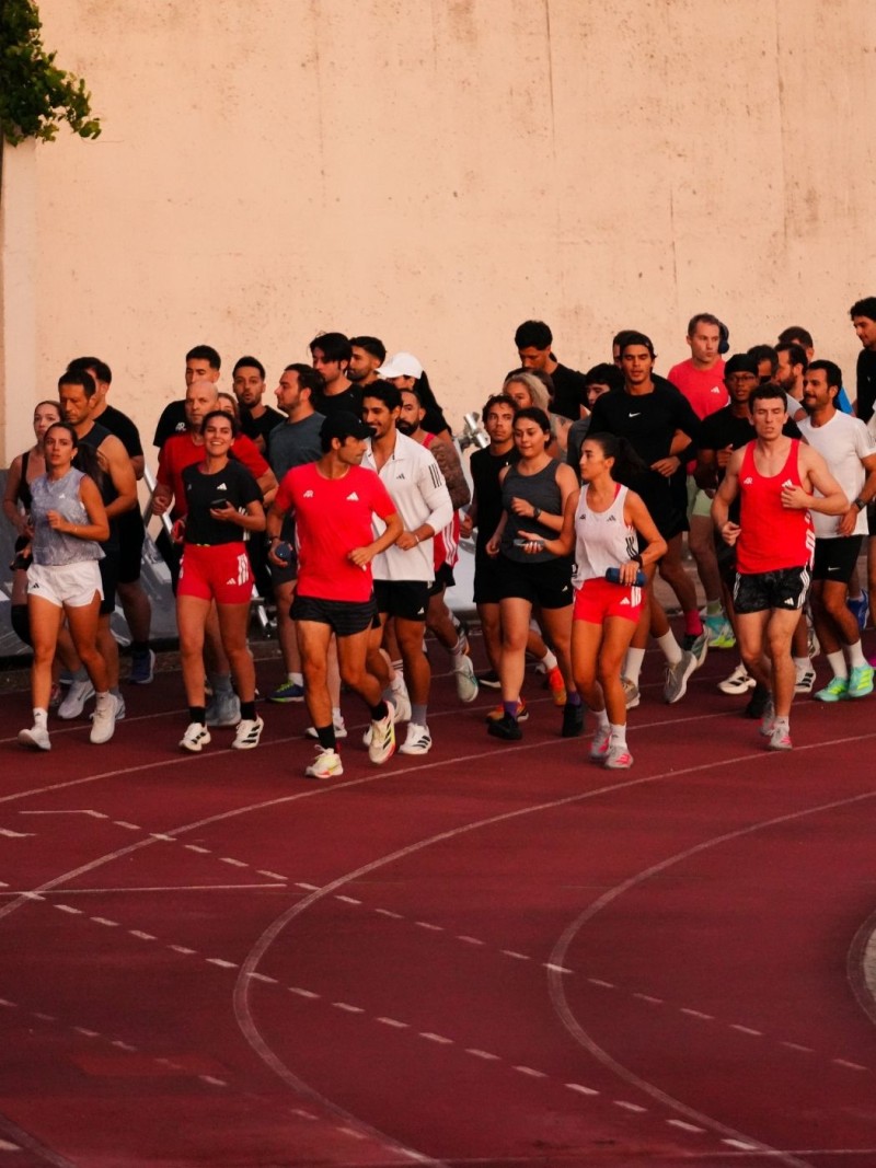 A group of people, mostly wearing red shirts, are running on a red track surrounded by a concrete wall in the background.