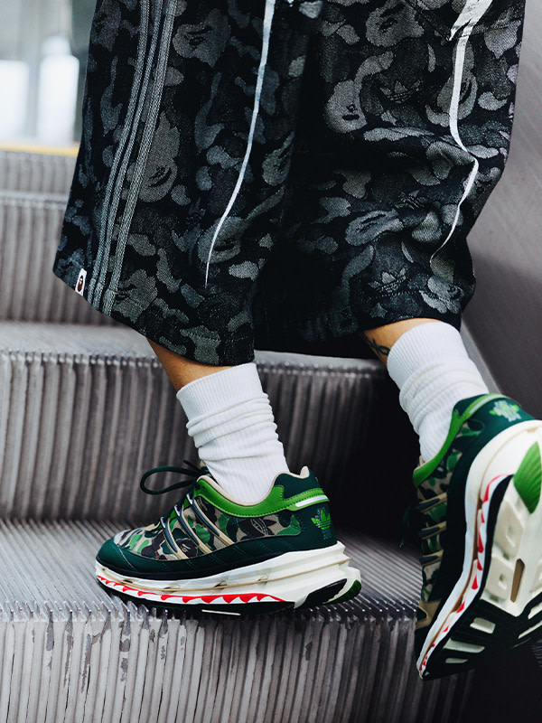The image shows a pair of colorful, patterned sneakers on a person's feet, with the person's legs and a radiator visible in the background.