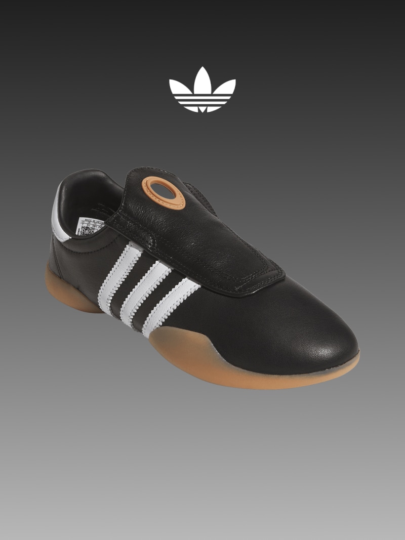 The image shows a pair of black and white Adidas sneakers with the iconic Adidas trefoil logo prominently displayed in the background.