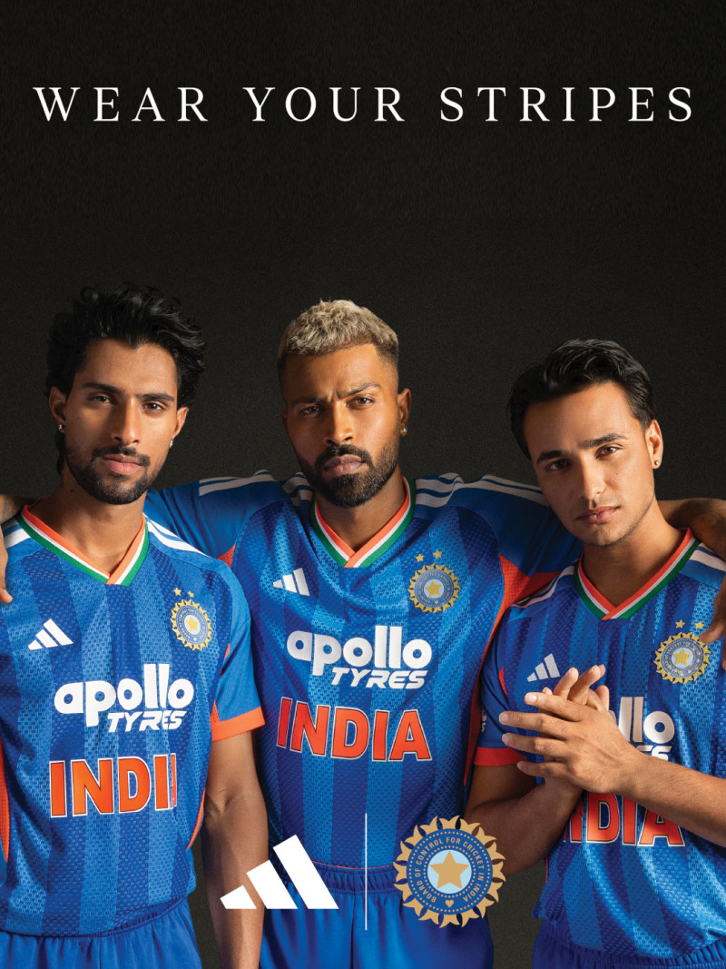 The image features three men wearing cricket jerseys with the text "INDIA" prominently displayed, standing against a dark background with the text "WEAR YOUR STRIPES" above them.