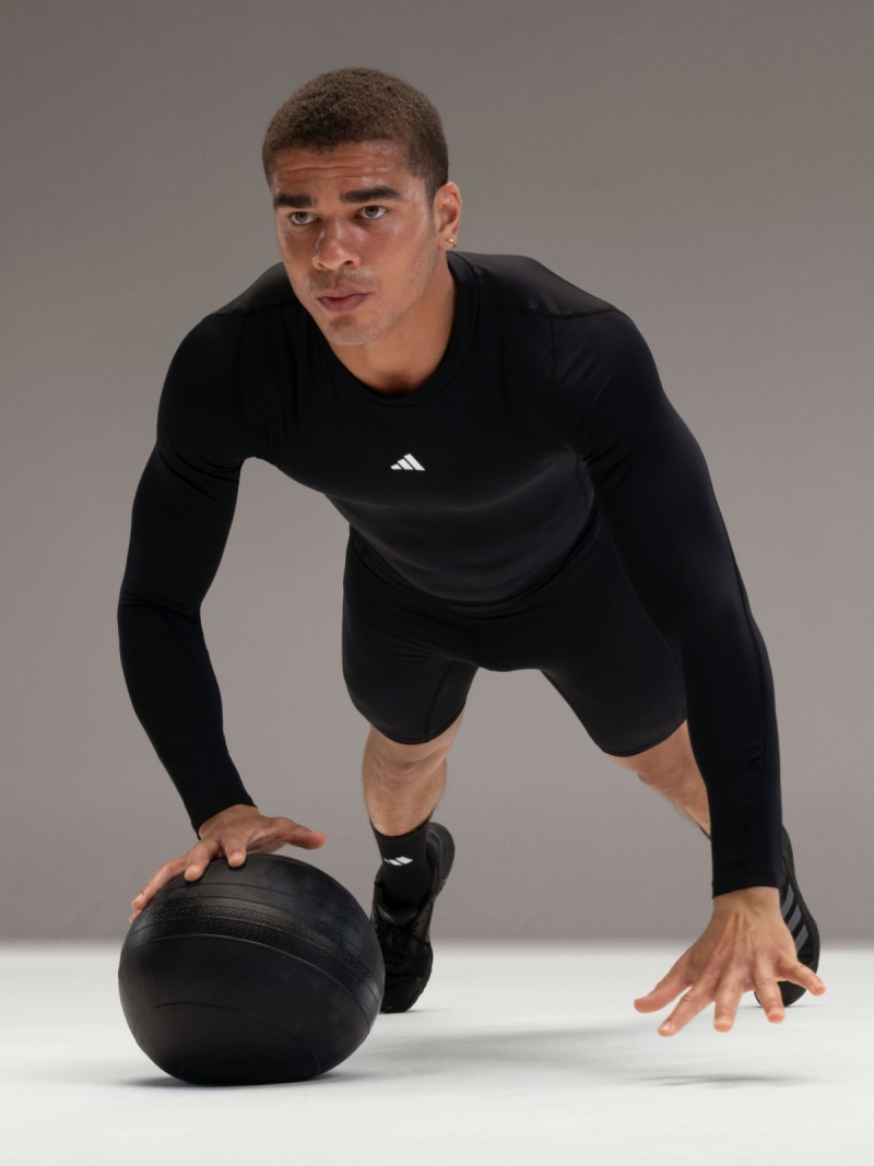 Man wearing adidas training gear performs press-ups with medicine ball.