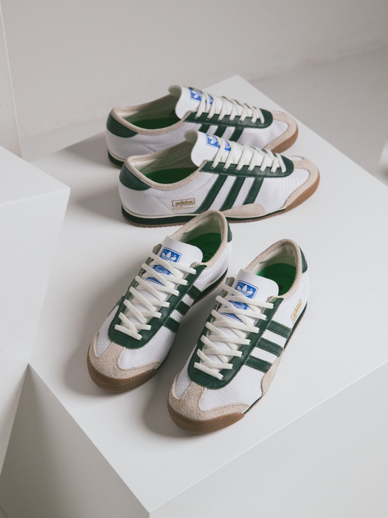 A pair of green and white Adidas sneakers are displayed on a white surface, with a simple and minimalist background.