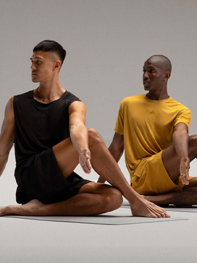 Two men in athletic wear sitting on the floor in a meditative pose against a plain background.
