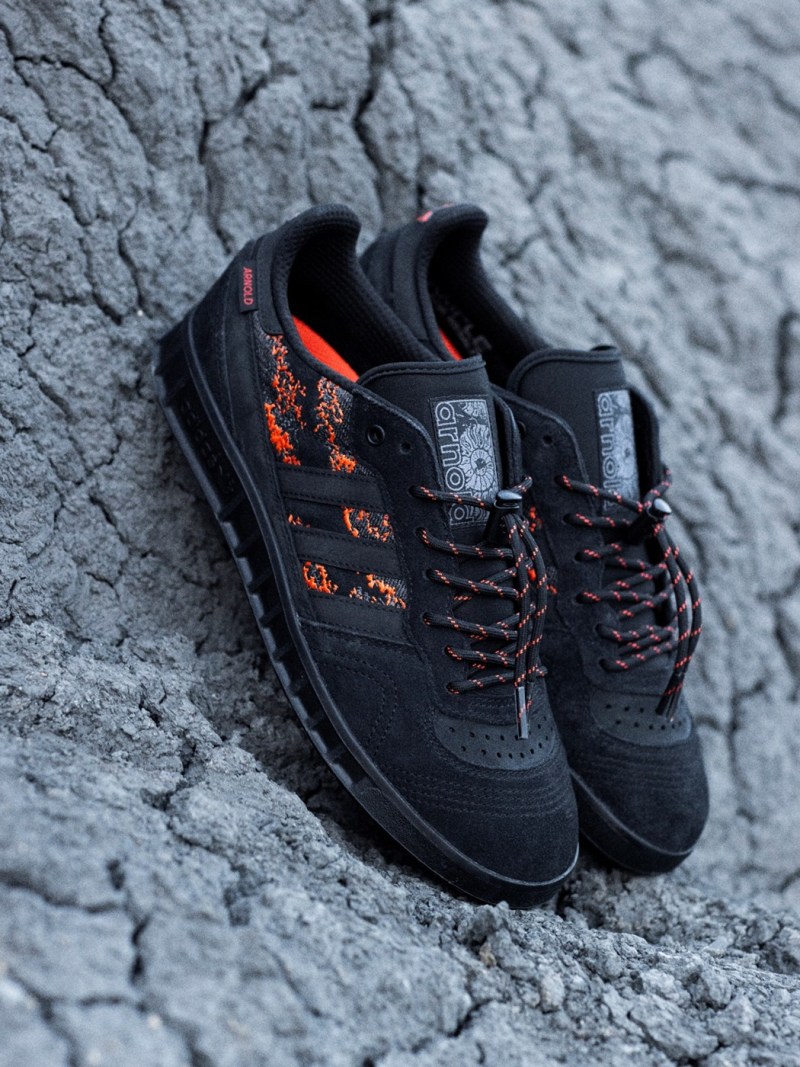 A pair of black and orange hiking shoes rests on a cracked, rocky surface against a gray, textured background.