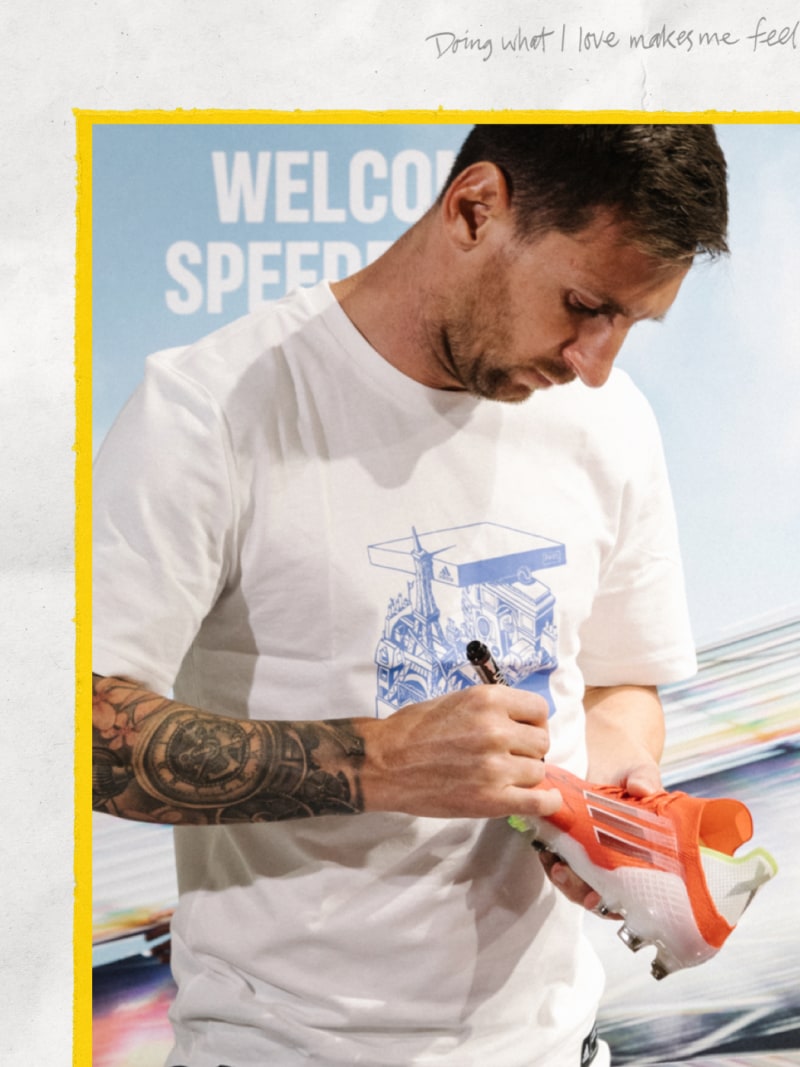 A man wearing a white t-shirt with a graphic design is holding an orange toy gun in the foreground, with a "Welcome Speed" sign visible in the background.
