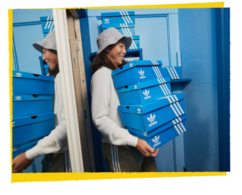 A woman carries 4 boxes of adidas sneakers on the background of a blue door