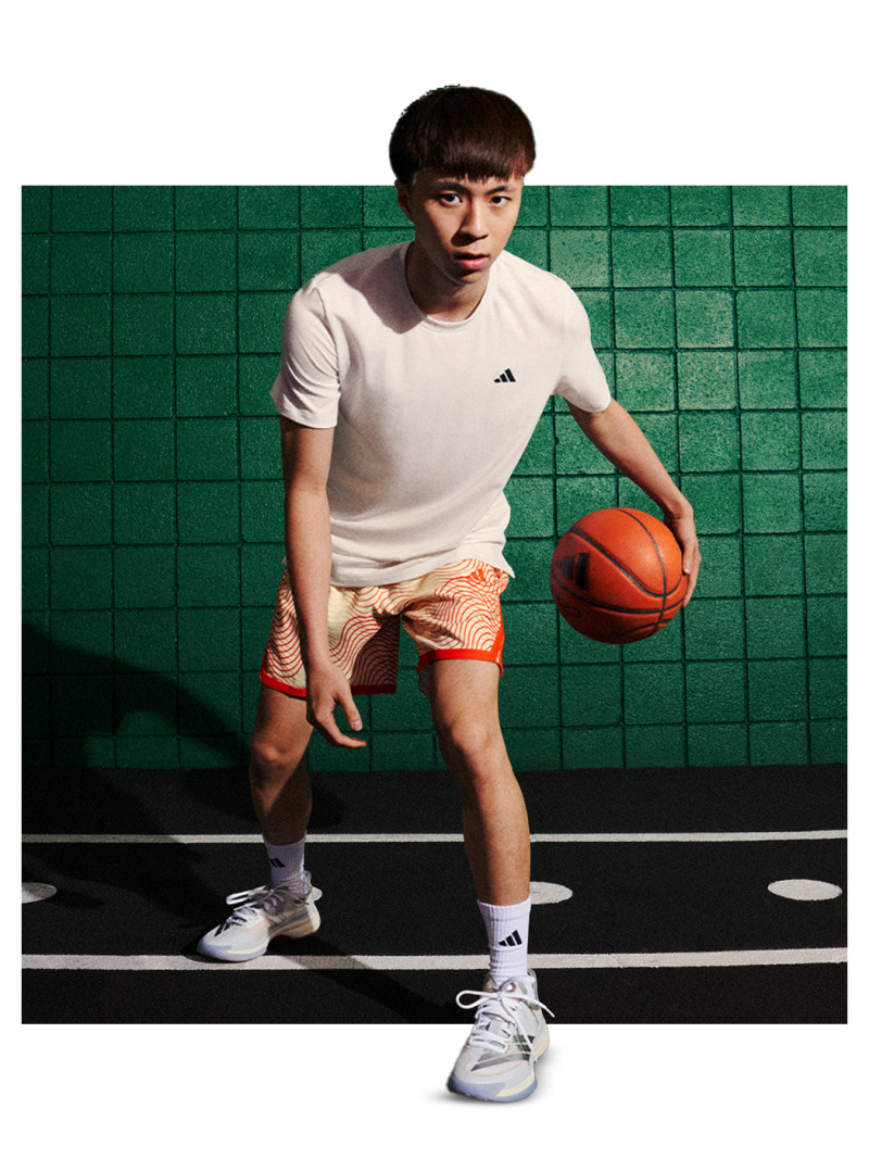 A young man in a white t-shirt and orange shorts stands on a basketball court, holding an orange basketball.