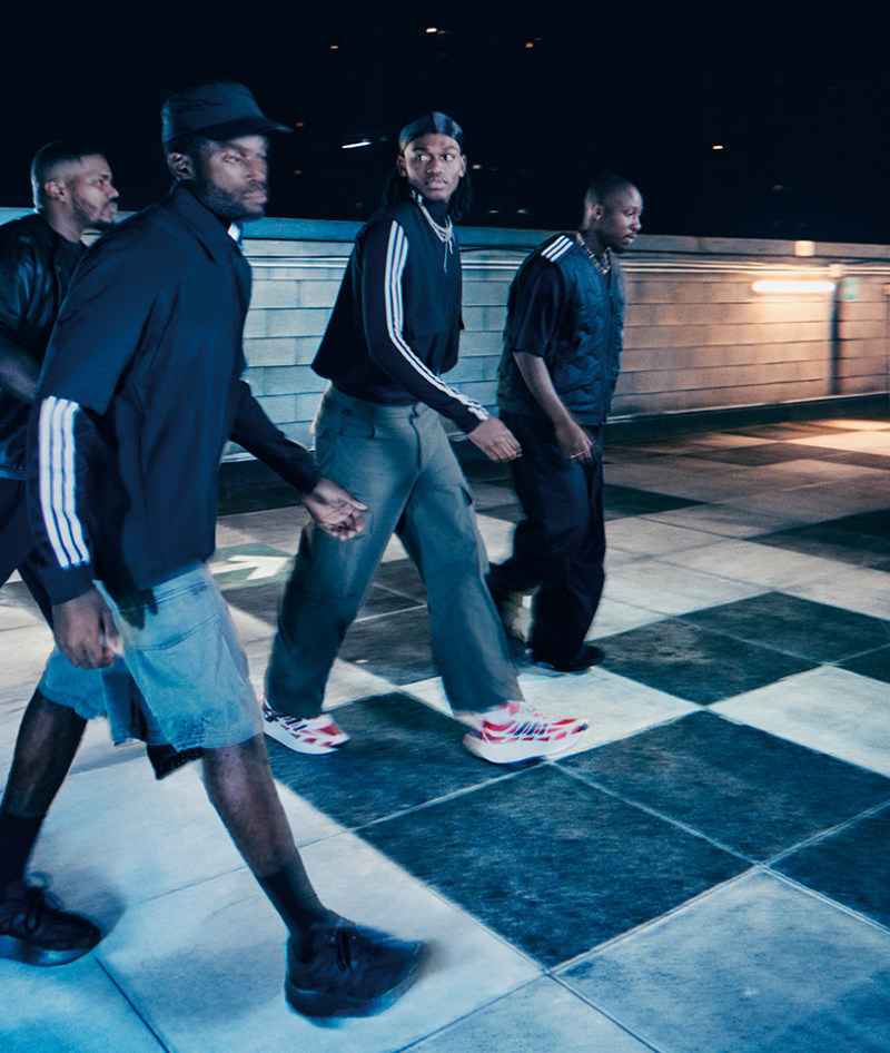 A group of young men standing on a tiled floor, with a wooden structure in the background, creating an urban, nighttime atmosphere.