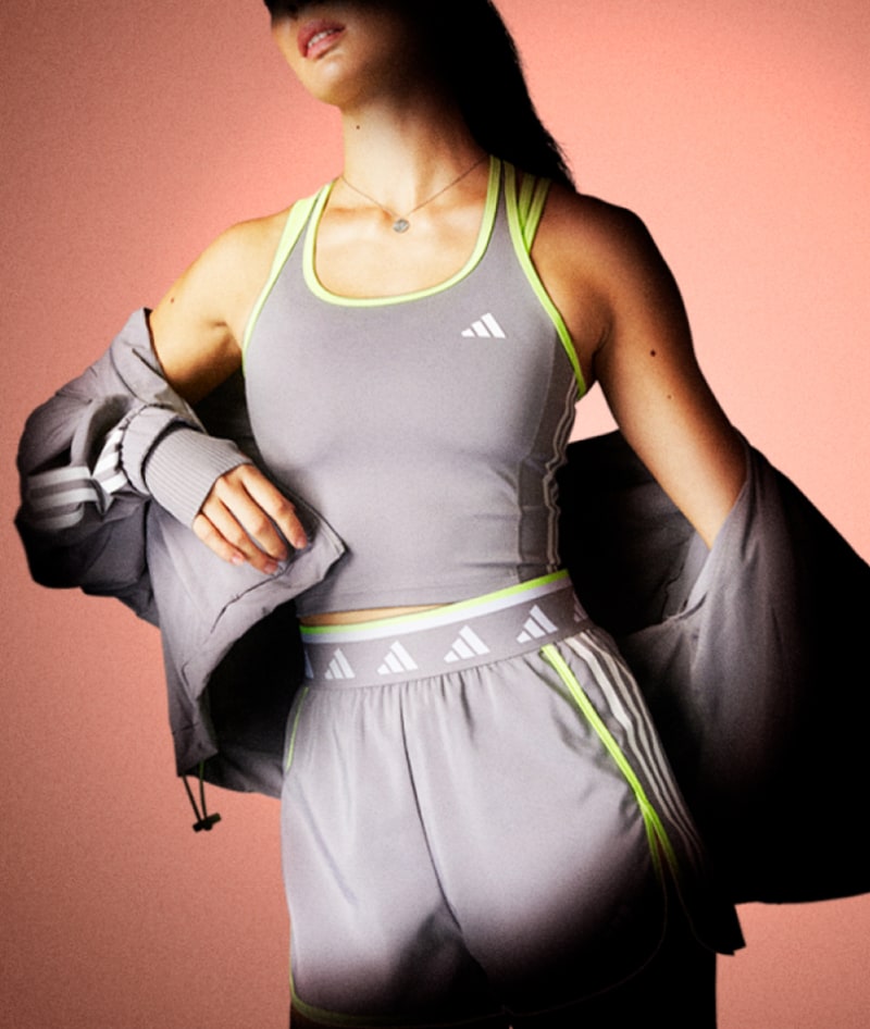 A person wearing a gray athletic outfit, including a sports bra and shorts, stands against a peach-colored background.