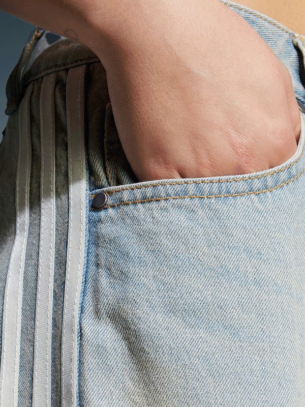 The image shows a close-up view of a person's hand resting on the waistband of a pair of light-colored denim jeans, with the background blurred.