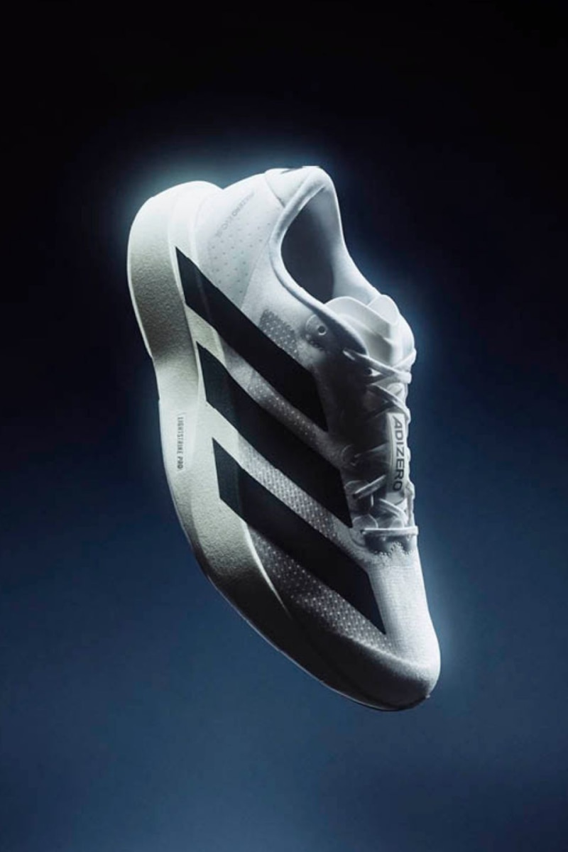 A white and black athletic shoe floats against a dark, moody background, its design and form prominently displayed.