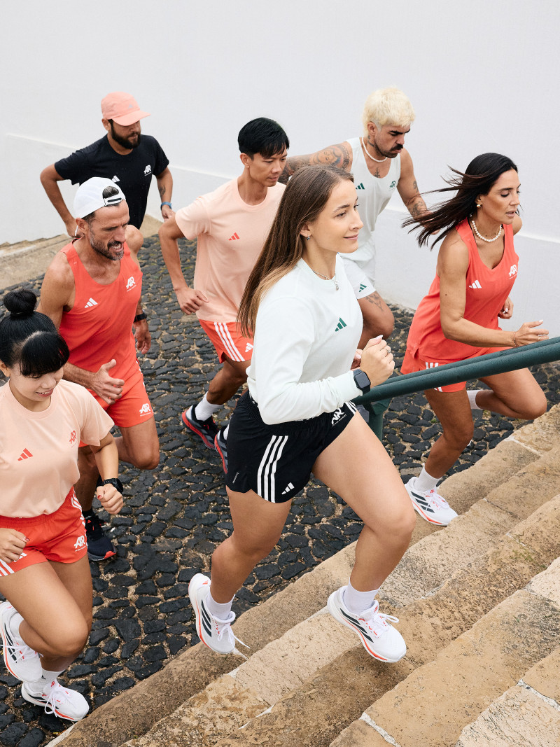 Seven people, three women and four men, running together up a staircase in an urban setting