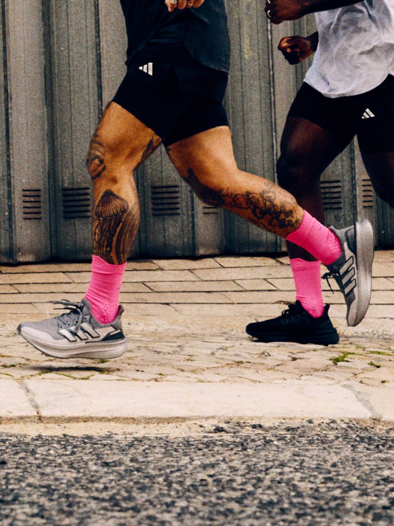 A group of people wearing athletic gear and running on a paved surface in front of a corrugated metal wall.