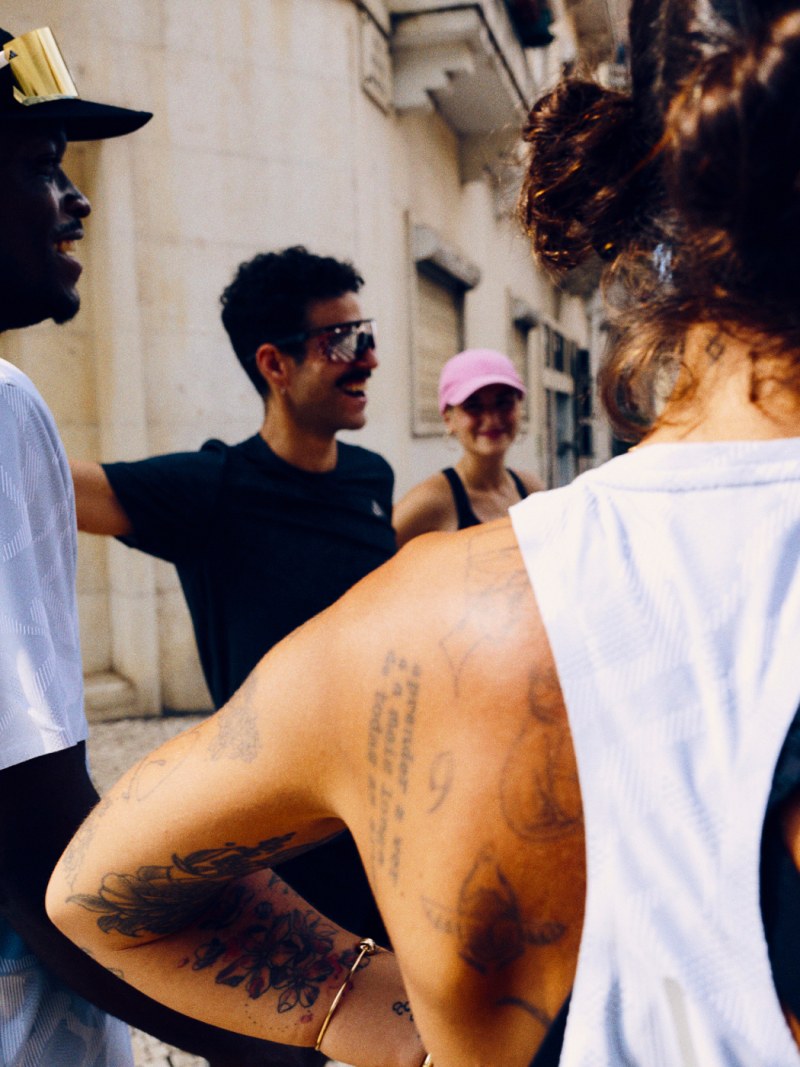 A group of people, some with tattoos, standing in an urban setting with buildings and structures visible in the background.