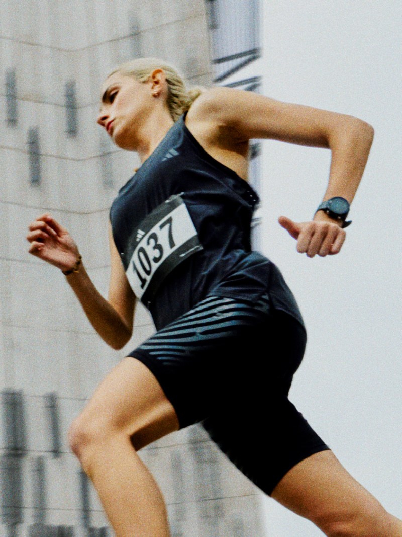 A woman in athletic wear is running in an urban setting, with tall buildings visible in the background.