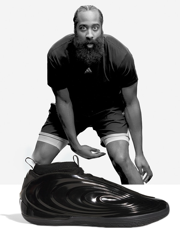 Image en noir et blanc d’un joueur de basketball assis en train de lacer ses chaussures, portant des vêtements de basketball adidas.